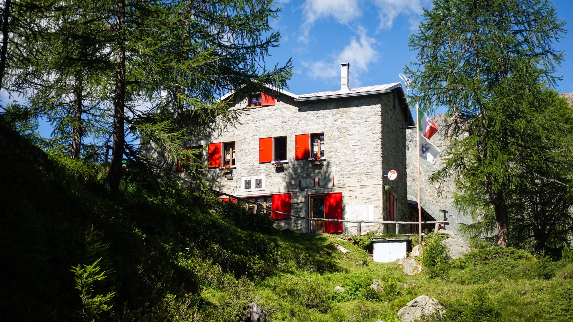Steinhütte mit roten Fensterläden im Wald